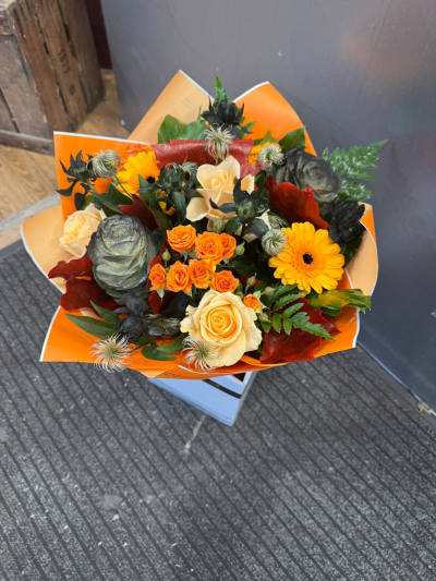 Autumn Sunset - A striking arrangement filled with vibrant orange, golden yellow and warm cream tones, beautifully complemented by rich seasonal foliage. Presented in a stylish gift bag, this eye-catching design captures the beauty of autumn and makes a wonderful gift for any special occasion.