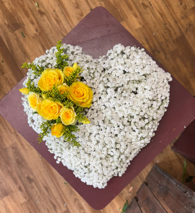Sunshine of My Heart - A beautiful heart-shaped funeral tribute featuring a delicate white base with a stunning cluster of sunshine yellow roses. This elegant arrangement symbolises warmth, love and cherished memories, offering a heartfelt way to say goodbye to someone who brought sunshine into your life.
