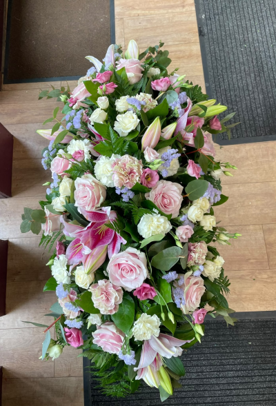 Gentle Pink Remembrance - An elegant, full-length funeral spray featuring a beautiful combination of soft pink, ivory and delicate lilac tones, complemented by lush greenery. This graceful arrangement offers a touching way to express love, sympathy and remembrance, creating a fitting farewell to someone special.