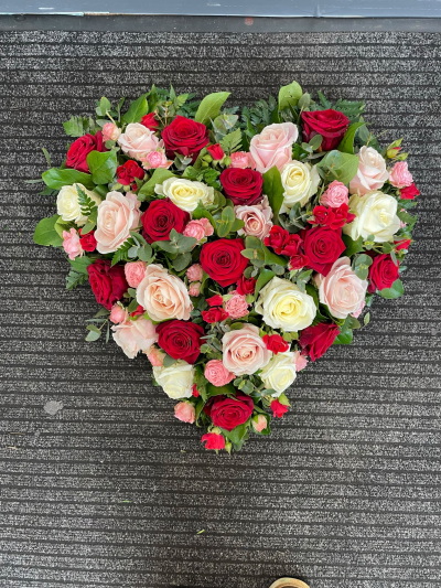 Endless Love Heart - A stunning heart-shaped funeral tribute featuring a beautiful combination of rich red, soft pink and ivory roses, complemented by fresh greenery. This romantic arrangement symbolises everlasting love and devotion, making it a meaningful final farewell to a cherished partner or loved one.